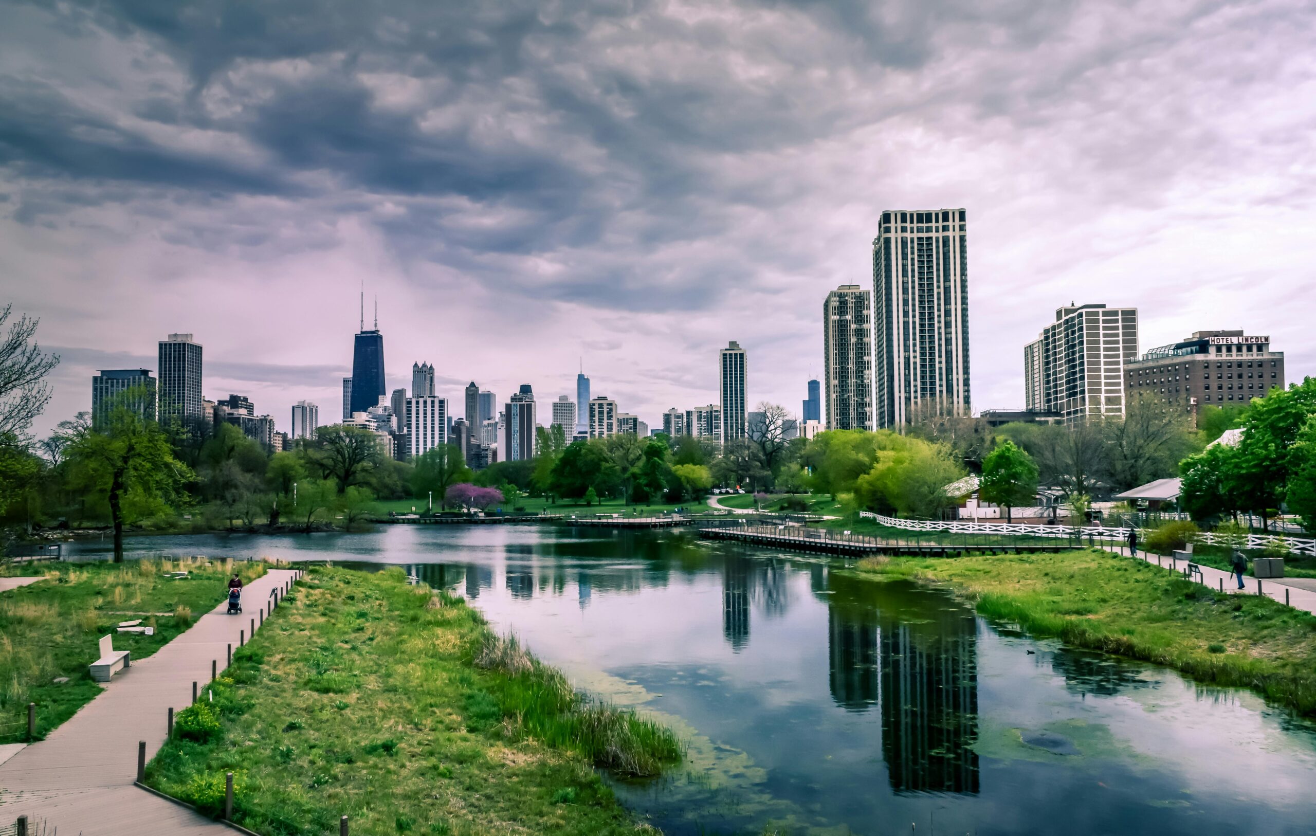Dramatic view of Chicago skyline with reflections over Lincoln Park Lagoon on a cloudy day.